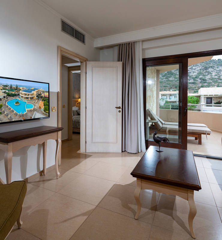 Hotel room with white color and gray wallpaper and gray curtains with a beige sofa with a green armchair two tables and a television
